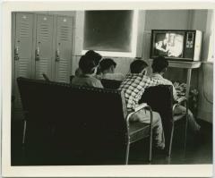 [Male students with back towards the camera watching TV]