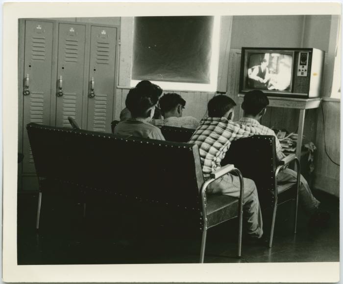 [Male students with back towards the camera watching TV]