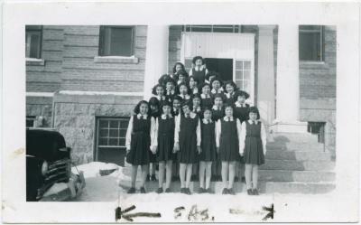 Ready for church in P. la P. [Portage la Prairie]. [Female students in school uniform standing in front of the school facade].