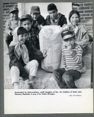 Surrounded by baby-watchers, small daughter of Rev. Art Veldhuis of God's Lake Narrows, Manitoba, is cosy in her Indian tikinagun