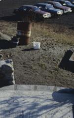 Stone wall of cairn with oil barrel used for waster and parking lot in distance as workmen build cairn to commemorate the Native apology of the United Church to the Native people for years of rejecting Native spirituality