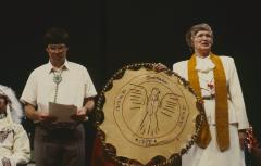 Anne Squire stands facing the council, holding gift presented to the United Church of Canada from the ANCC after the constitution of the ANCC and covenanting service at the 32nd General Council.