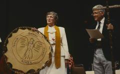 Anne Squire holding the gift presented to the United Church of Canada by the ANCC, speaking to the delegates to the 32nd General Council. Howie Mills stands beside her holding talking stick after the service.