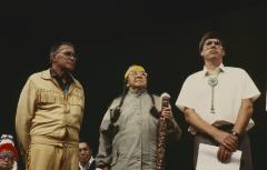 Alf Dumont, Gladys Taylor and Murray Whetung standing on platform at the 32nd General Council after the constitution and covenanting service.