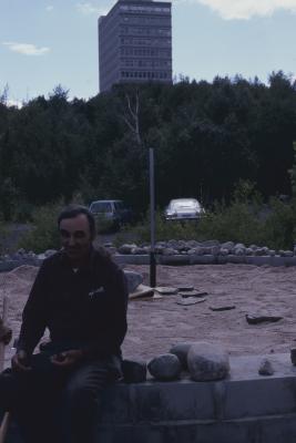 Elder Art Solomon seated on stone cairn, smiling facing camera