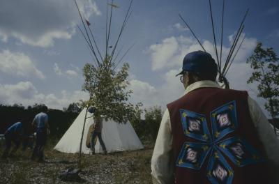 Moses Wood, wearing a vest with native art on back, admiring the tepees just erected during the afternoon of General Council, on ground adjacent (part of) University where the Council was held