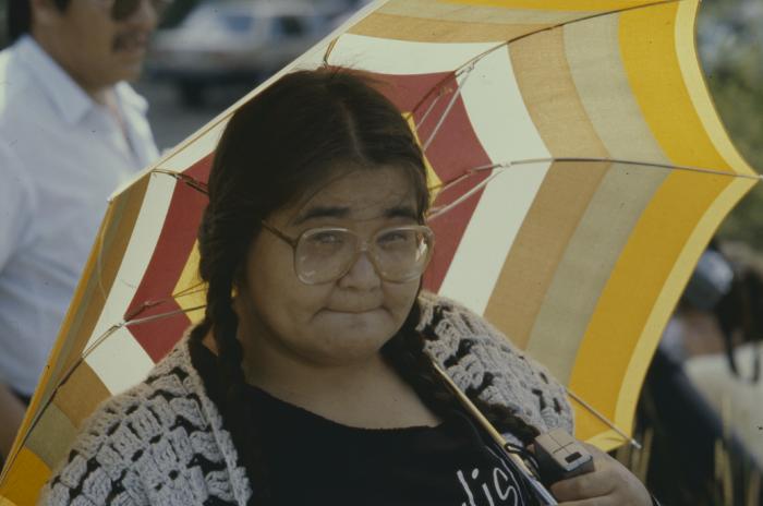 April Reid holds umbrella protects herself from the hot sun waiting for the gathering and the formal apology of the 31st General Council to the Native people.