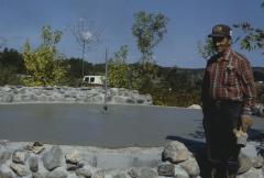 Elder Art Solomon standing beside the stone circular finished wall which will hold the stone cairn